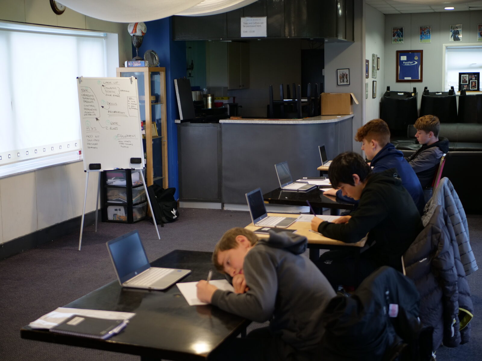 Young people working at tables with laptops and worksheets during an Alternative Provision session